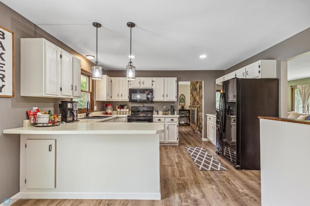 kitchen with decorative light fixtures, sink, black appliances, light hardwood / wood-style flooring, and kitchen peninsula