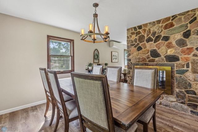 dining space featuring a stone fireplace, hardwood / wood-style floors, a wall mounted air conditioner, and a chandelier