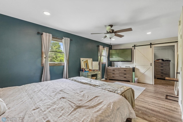 bedroom with light wood-type flooring, a barn door, and ceiling fan