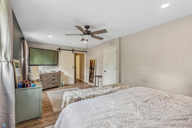 bedroom featuring ceiling fan, a barn door, and dark wood-type flooring