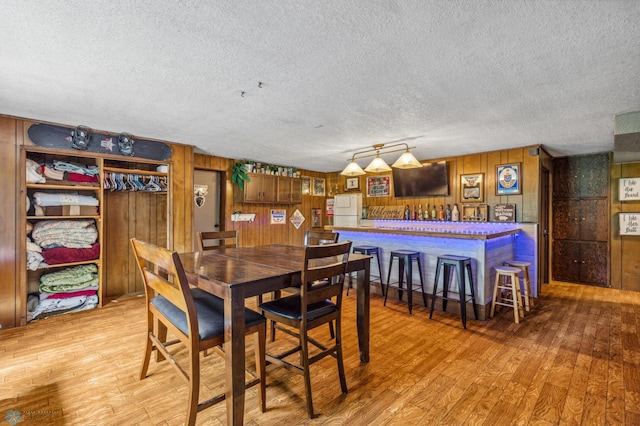 dining space featuring light wood-type flooring, a textured ceiling, track lighting, indoor bar, and wood walls