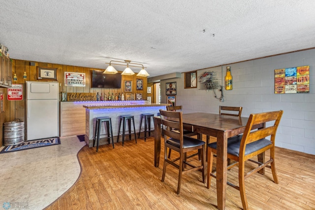 dining area with a textured ceiling, light hardwood / wood-style flooring, track lighting, and bar