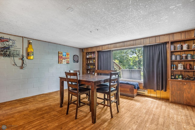 dining room featuring a baseboard heating unit, light hardwood / wood-style flooring, and a textured ceiling