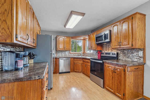 kitchen with sink, backsplash, a textured ceiling, stainless steel appliances, and light hardwood / wood-style flooring