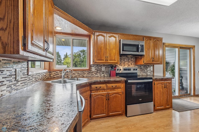 kitchen with backsplash, a textured ceiling, light wood-type flooring, sink, and stainless steel appliances