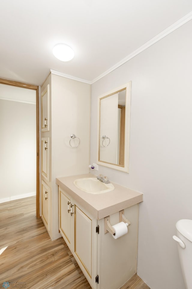 bathroom with toilet, ornamental molding, vanity, and wood-type flooring