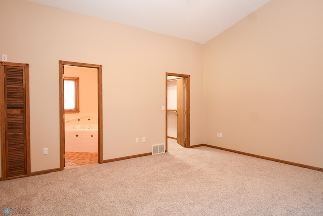 unfurnished bedroom with a closet, lofted ceiling, light colored carpet, connected bathroom, and a walk in closet