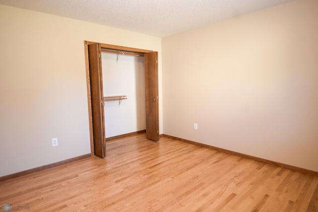 unfurnished bedroom with a textured ceiling, light hardwood / wood-style floors, and a closet