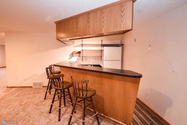 bar with a textured ceiling, carpet, and white fridge