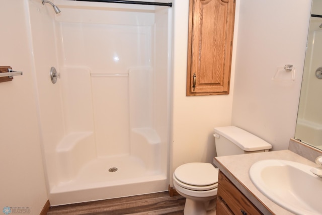 bathroom featuring wood-type flooring, walk in shower, vanity, and toilet