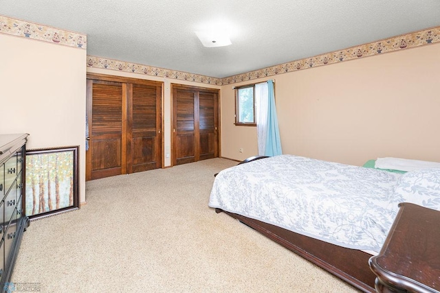 bedroom featuring two closets, a textured ceiling, and carpet flooring