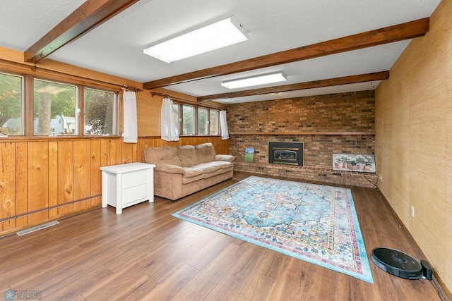 living room with wood walls, dark hardwood / wood-style flooring, a brick fireplace, beamed ceiling, and brick wall