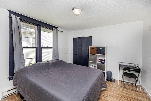 bedroom featuring a baseboard heating unit, a textured ceiling, multiple windows, and light hardwood / wood-style floors