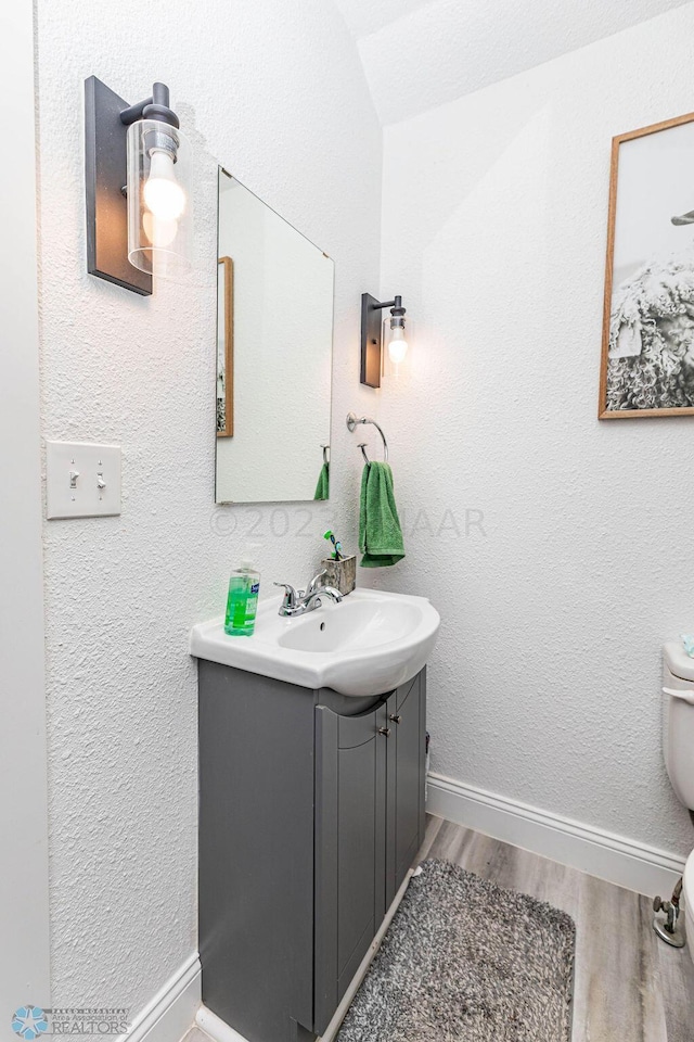 bathroom with lofted ceiling, hardwood / wood-style flooring, vanity, and toilet