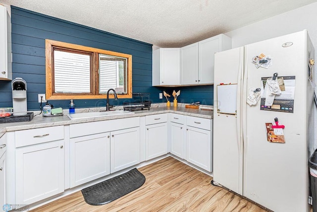 kitchen with white cabinets, wooden walls, white refrigerator with ice dispenser, and light hardwood / wood-style floors