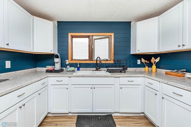 kitchen with light wood-type flooring, sink, a textured ceiling, and white cabinets