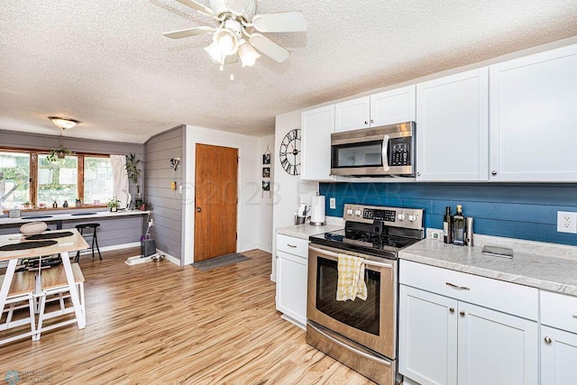 kitchen featuring light wood-type flooring, a textured ceiling, stainless steel appliances, white cabinetry, and ceiling fan