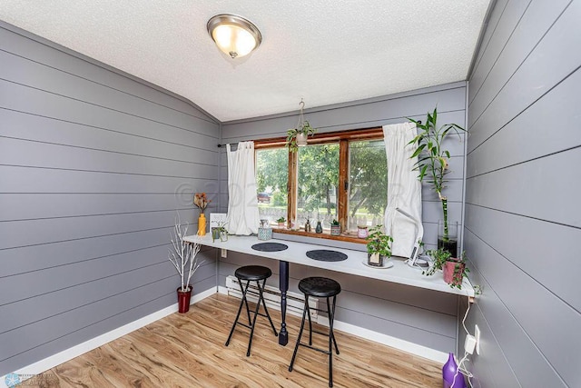 home office featuring wood walls, a textured ceiling, lofted ceiling, and light hardwood / wood-style floors