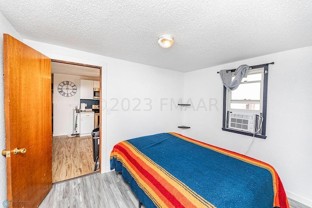 bedroom with cooling unit, a textured ceiling, and light hardwood / wood-style floors