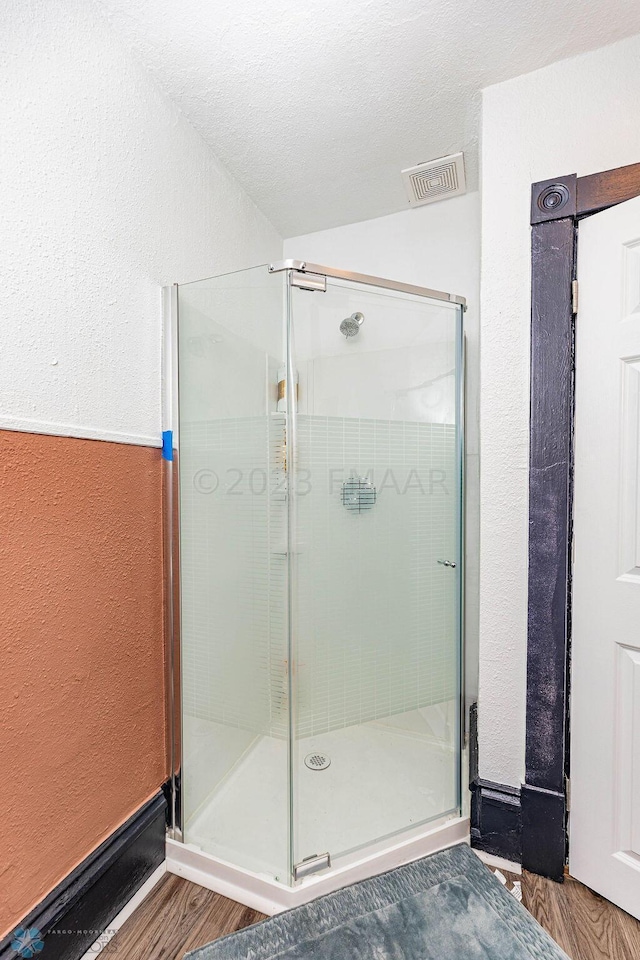 bathroom featuring a shower with shower door, wood-type flooring, and a textured ceiling