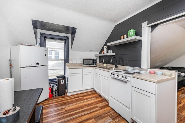 kitchen featuring lofted ceiling, white appliances, hardwood / wood-style floors, sink, and white cabinetry