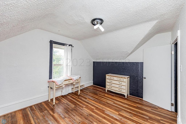 additional living space with wood-type flooring, vaulted ceiling, and a textured ceiling