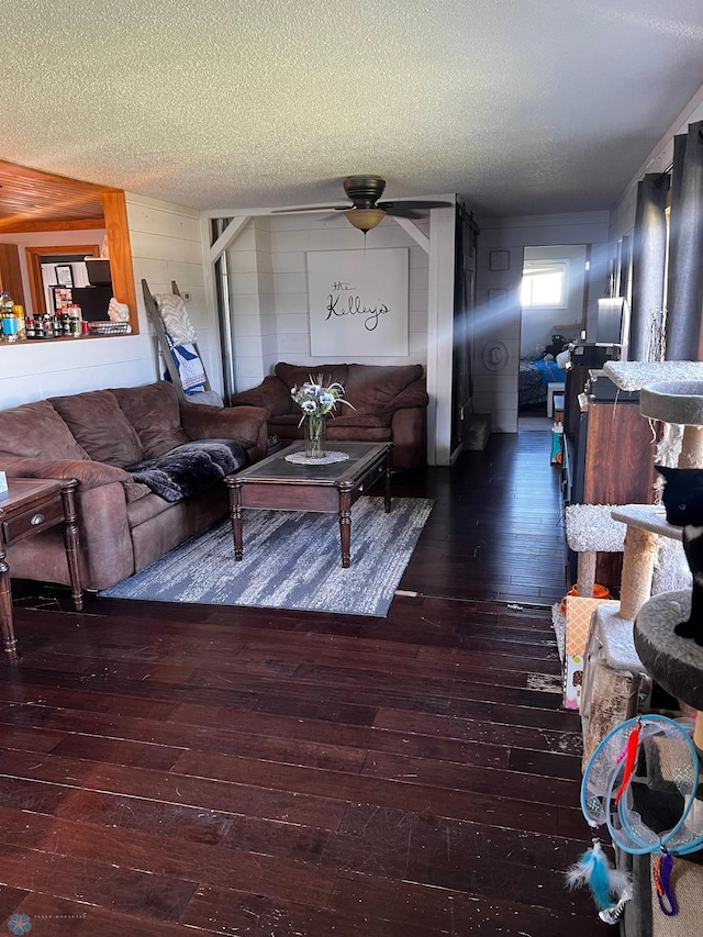 living room with wood walls, ceiling fan, dark wood-type flooring, and a textured ceiling