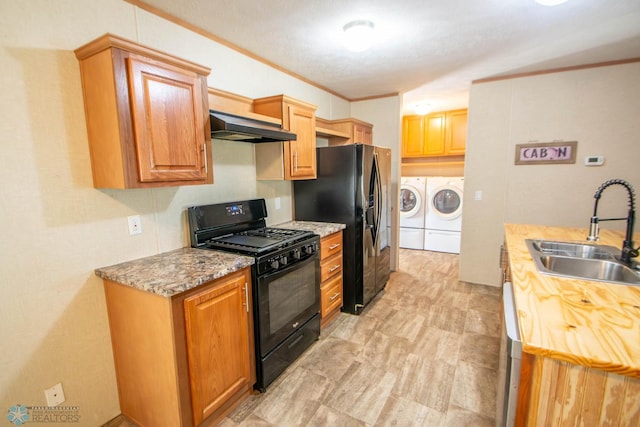 kitchen with wall chimney exhaust hood, independent washer and dryer, light tile patterned floors, sink, and black appliances