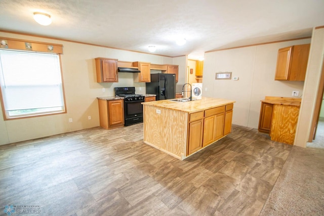 kitchen featuring sink, a center island with sink, black appliances, washer / dryer, and light carpet