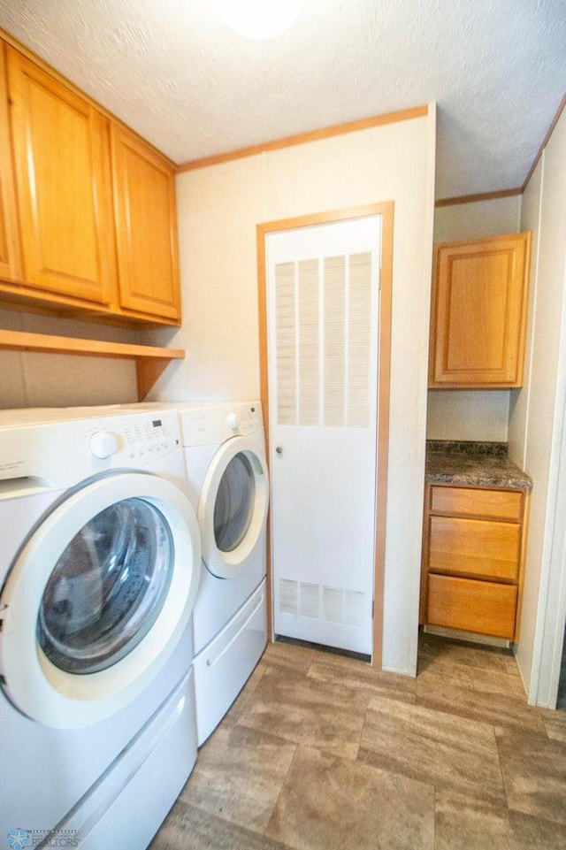 laundry area with washing machine and dryer, a textured ceiling, cabinets, and ornamental molding