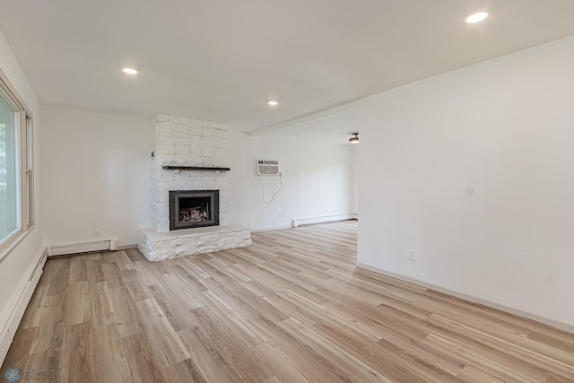 unfurnished living room with a fireplace, baseboard heating, light hardwood / wood-style floors, and an AC wall unit