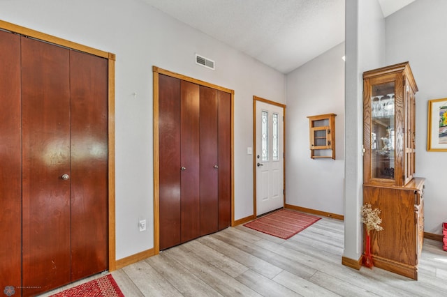 entryway with a textured ceiling, lofted ceiling, and light hardwood / wood-style floors