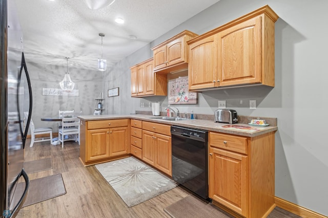 kitchen with black dishwasher, sink, decorative light fixtures, light hardwood / wood-style floors, and stainless steel fridge