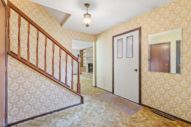 entryway with carpet floors, brick wall, a textured ceiling, and a brick fireplace