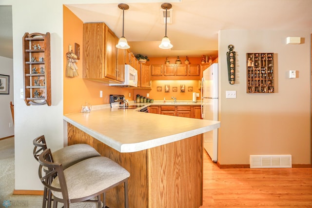 kitchen featuring light wood-type flooring, sink, decorative light fixtures, kitchen peninsula, and white appliances