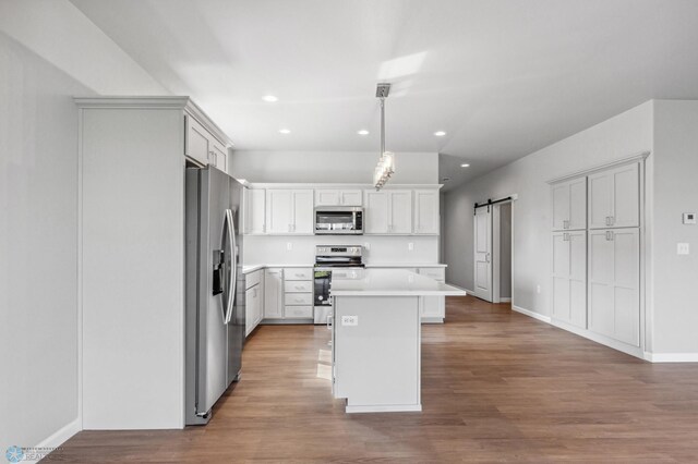 kitchen with light hardwood / wood-style flooring, a kitchen island, hanging light fixtures, a barn door, and appliances with stainless steel finishes