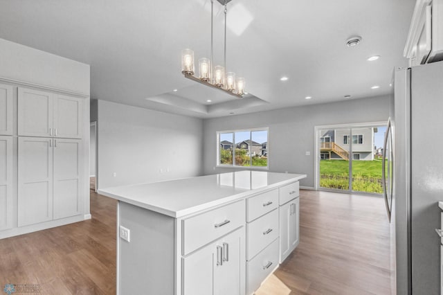 kitchen featuring decorative light fixtures, light wood-type flooring, stainless steel refrigerator, a kitchen island, and a tray ceiling