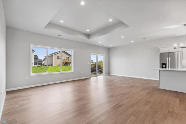 unfurnished living room with a tray ceiling, light hardwood / wood-style floors, and a chandelier