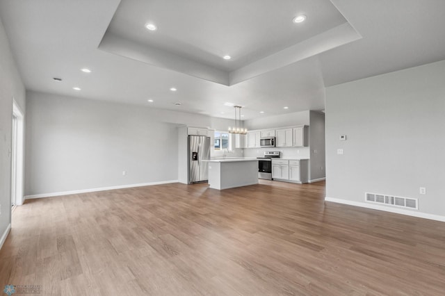 unfurnished living room with light wood-type flooring, a chandelier, sink, and a tray ceiling