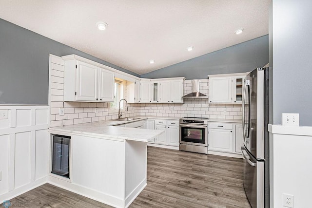 kitchen with stainless steel appliances, vaulted ceiling, wall chimney range hood, and hardwood / wood-style flooring