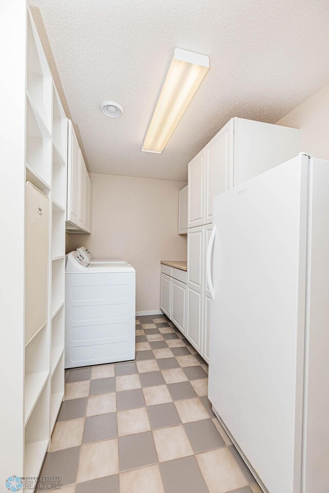 clothes washing area with washer / clothes dryer, light tile patterned flooring, a textured ceiling, and cabinets