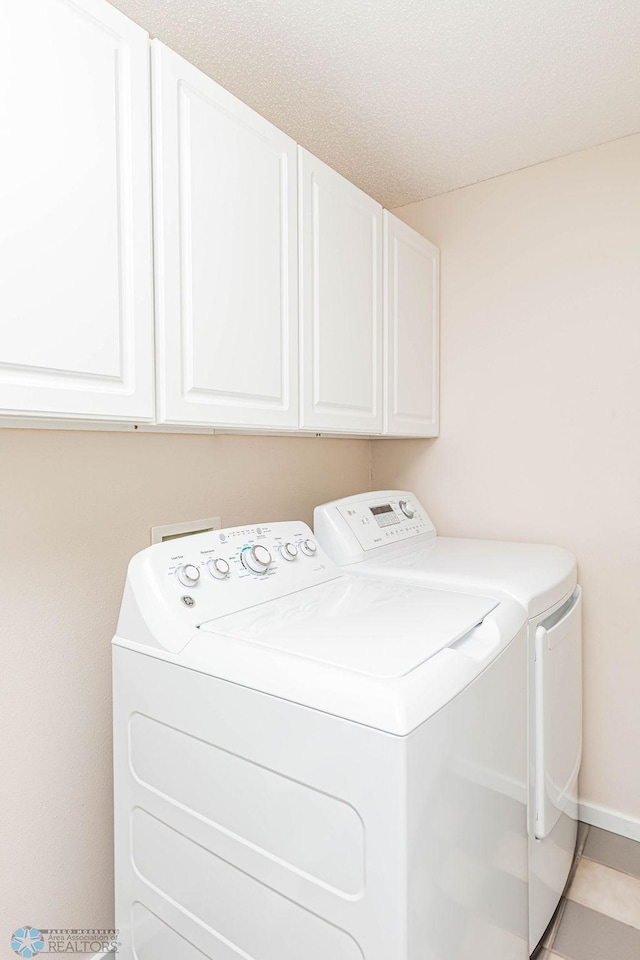 laundry area with washing machine and dryer, cabinets, and light tile patterned floors