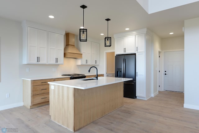 kitchen featuring light hardwood / wood-style floors, custom exhaust hood, a center island with sink, and white cabinets