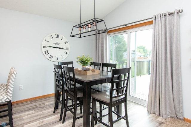 dining space with an inviting chandelier, vaulted ceiling, and light hardwood / wood-style flooring