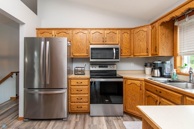 kitchen featuring sink, light wood-type flooring, vaulted ceiling, and stainless steel appliances