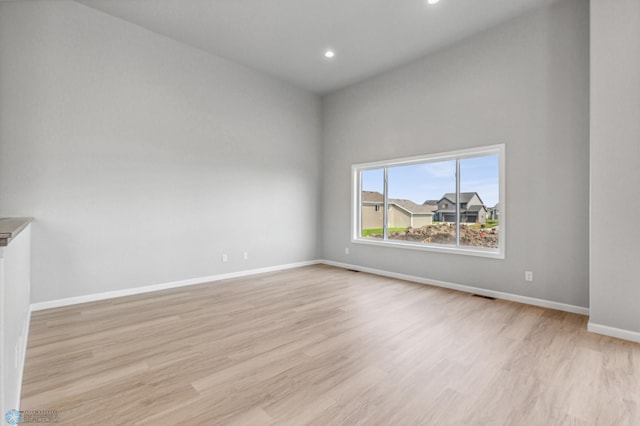 empty room with a towering ceiling and light hardwood / wood-style flooring