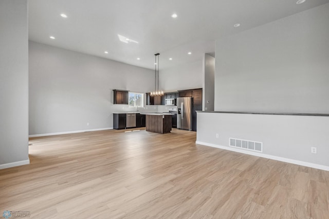 unfurnished living room featuring light hardwood / wood-style floors, a high ceiling, and a chandelier