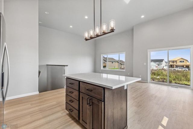 kitchen featuring an inviting chandelier, light hardwood / wood-style flooring, dark brown cabinets, a kitchen island, and hanging light fixtures