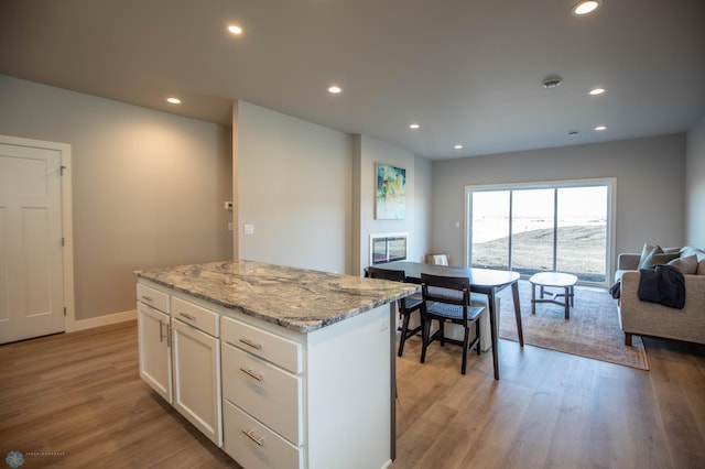 kitchen featuring light wood-type flooring, white cabinetry, light stone countertops, and a kitchen island