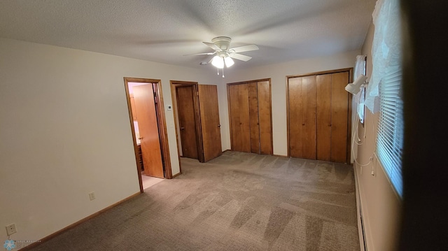 unfurnished bedroom with a textured ceiling, ceiling fan, two closets, and light carpet